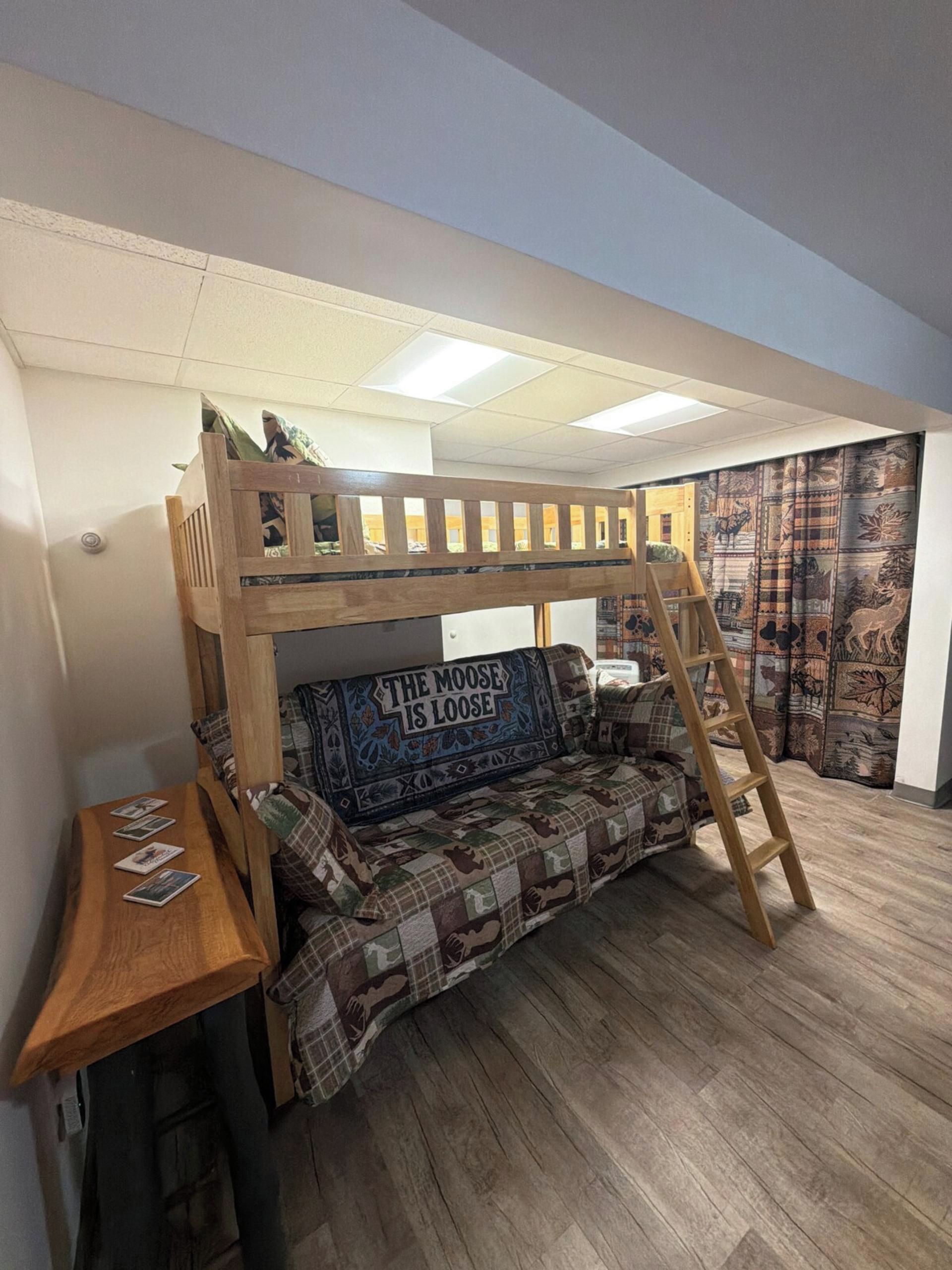 A bunk bed with a ladder, a small table with a book, and a wall with a moose-themed design.