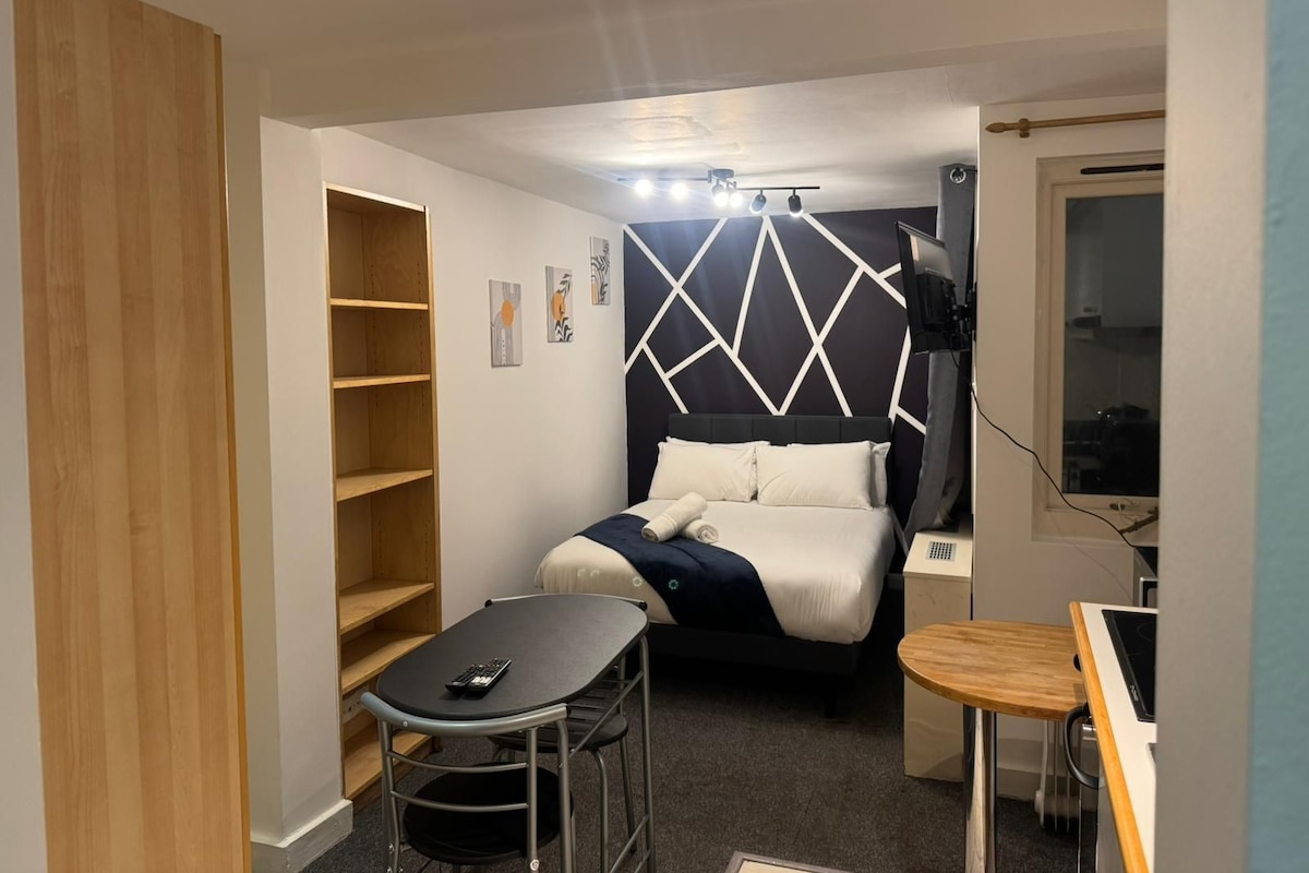 Una habitación de hotel pequeña con una cama, una mesita, una silla, un escritorio y un armario.