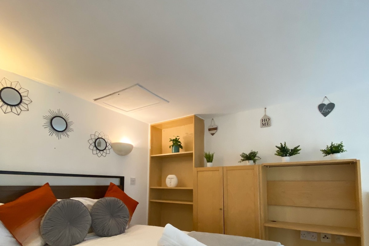 Una cama bien hecha con almohadas, una mesita de noche con lámpara, un armario y decoración en la pared.