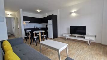 Een moderne woonkamer met een grijze bank, een klein wit tafeltje en een televisie op een witte dressoir.