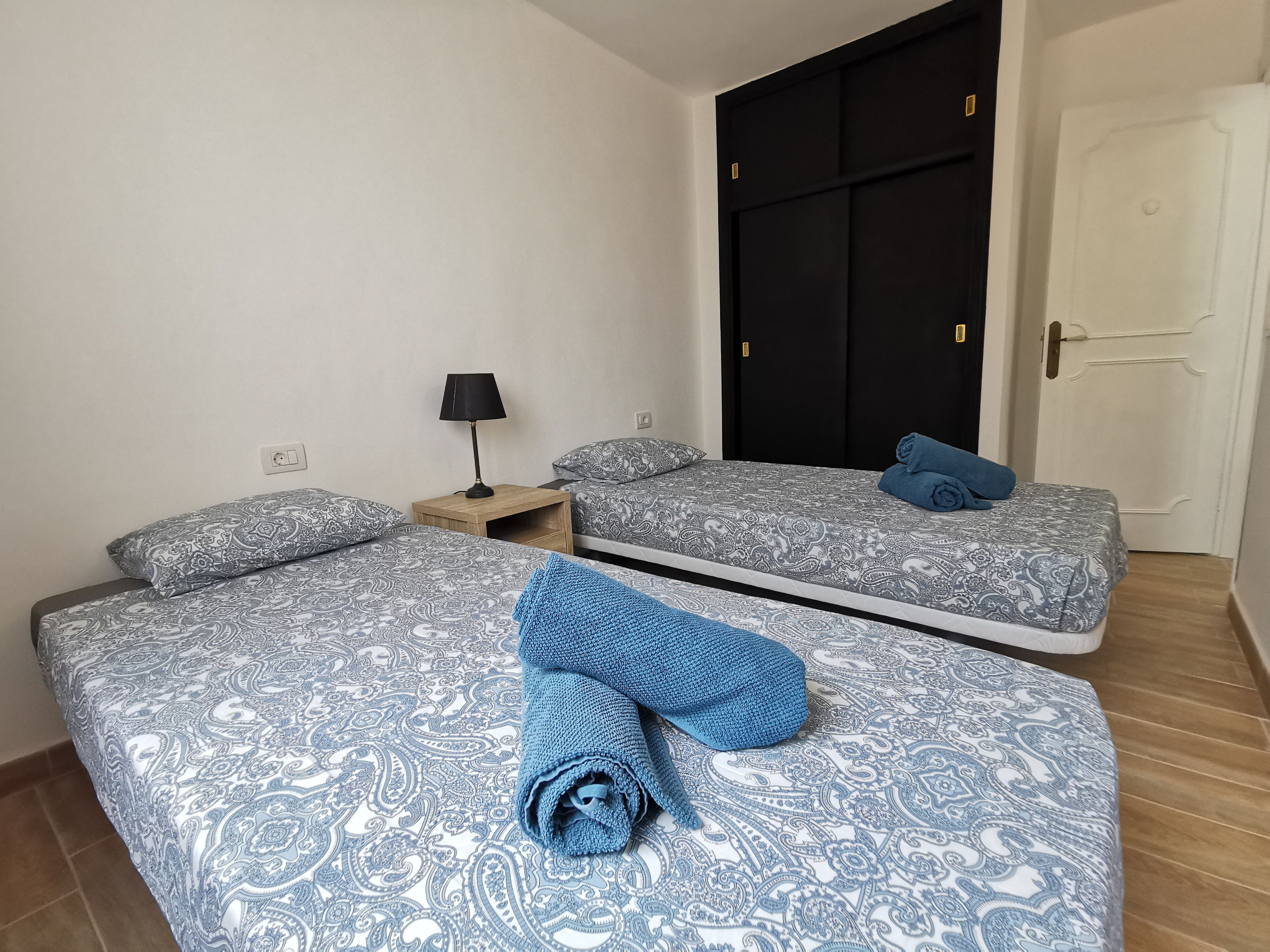 Een hotelkamer met twee bedden, een nachtkastje met een lamp en een garderobe.