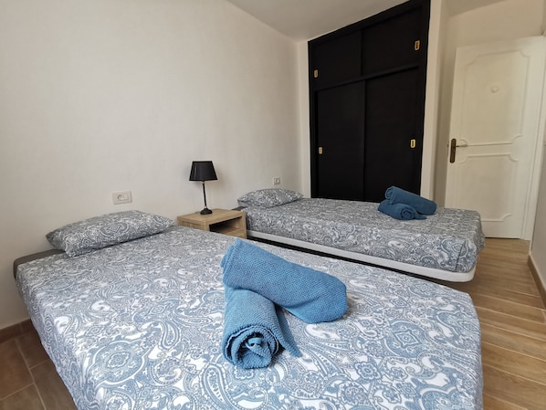 Een hotelkamer met twee bedden, een nachtkastje met een lamp en een garderobe.