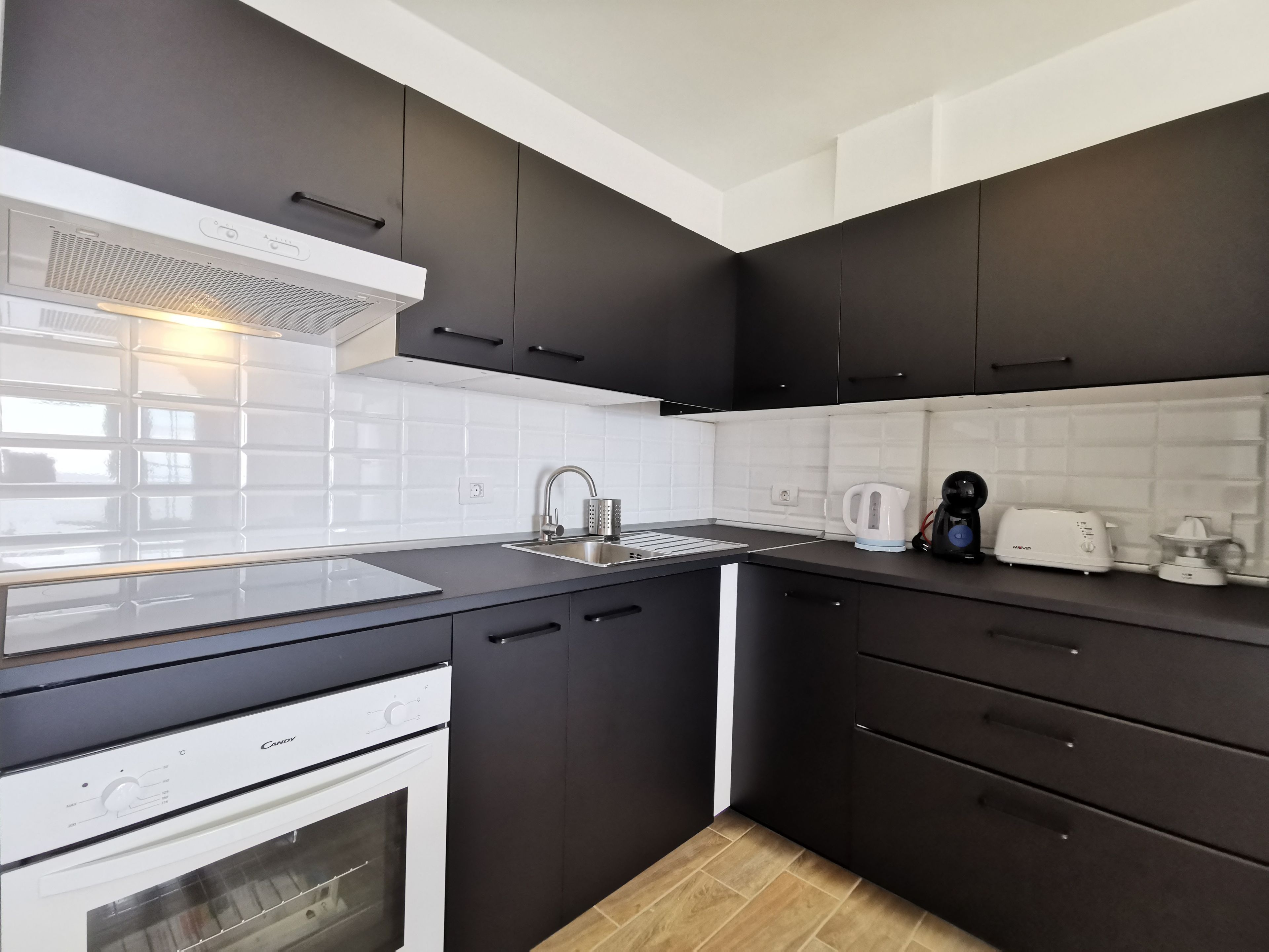Een moderne keuken met donkere kastjes, een wit aanrecht, een ingebouwde oven en een koffiezetapparaat.