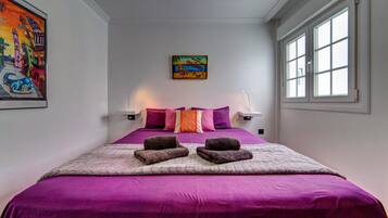 Een slaapkamer met een groot bed, twee bedlampen, een schilderij aan de muur en een raam met zonwering.