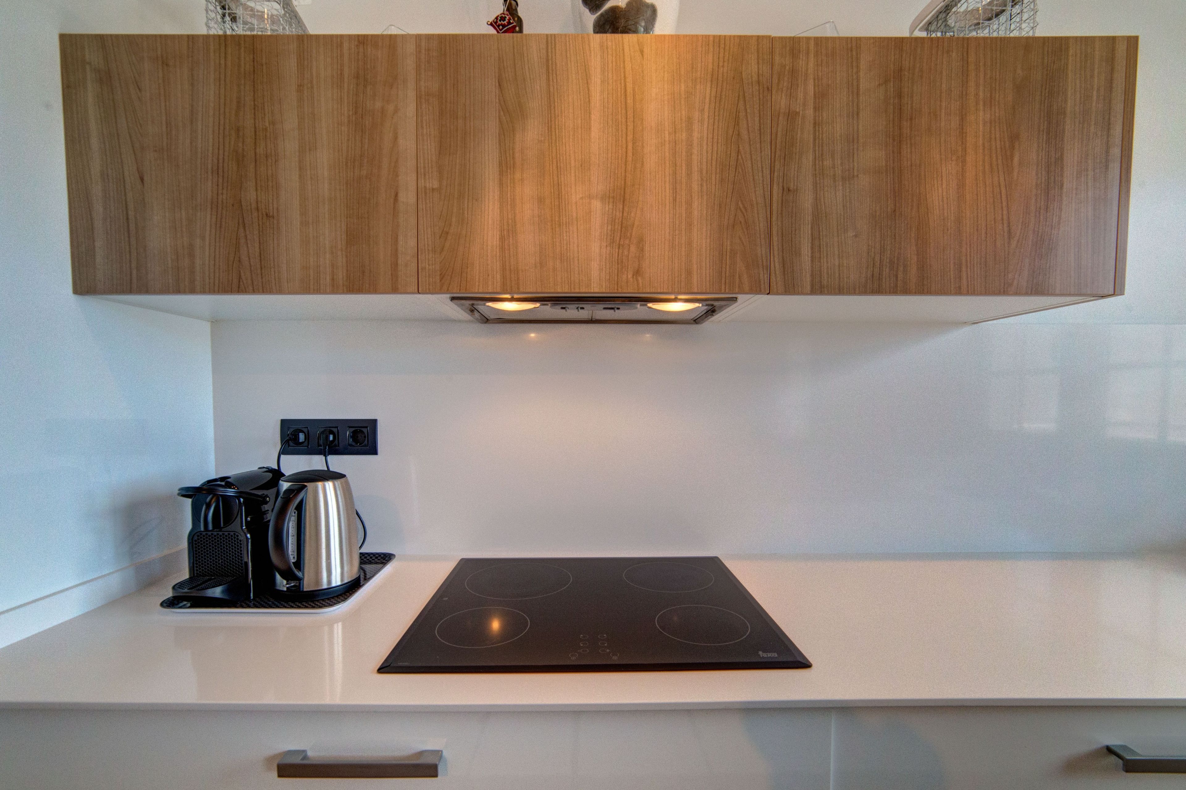 Eine moderne Küche mit einem Holzkasten über einer weißen Arbeitsplatte, einer schwarzen Induktionskochplatte und einer Kaffeemaschine.