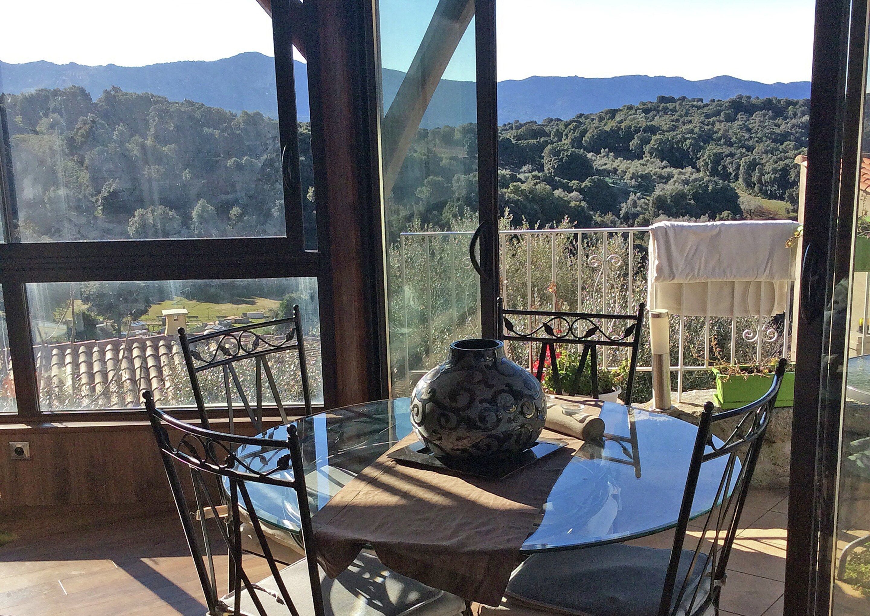 A glass table with chairs and a decorative vase, overlooking a mountainous landscape.