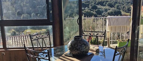 A glass table with chairs and a decorative vase, overlooking a mountainous landscape.