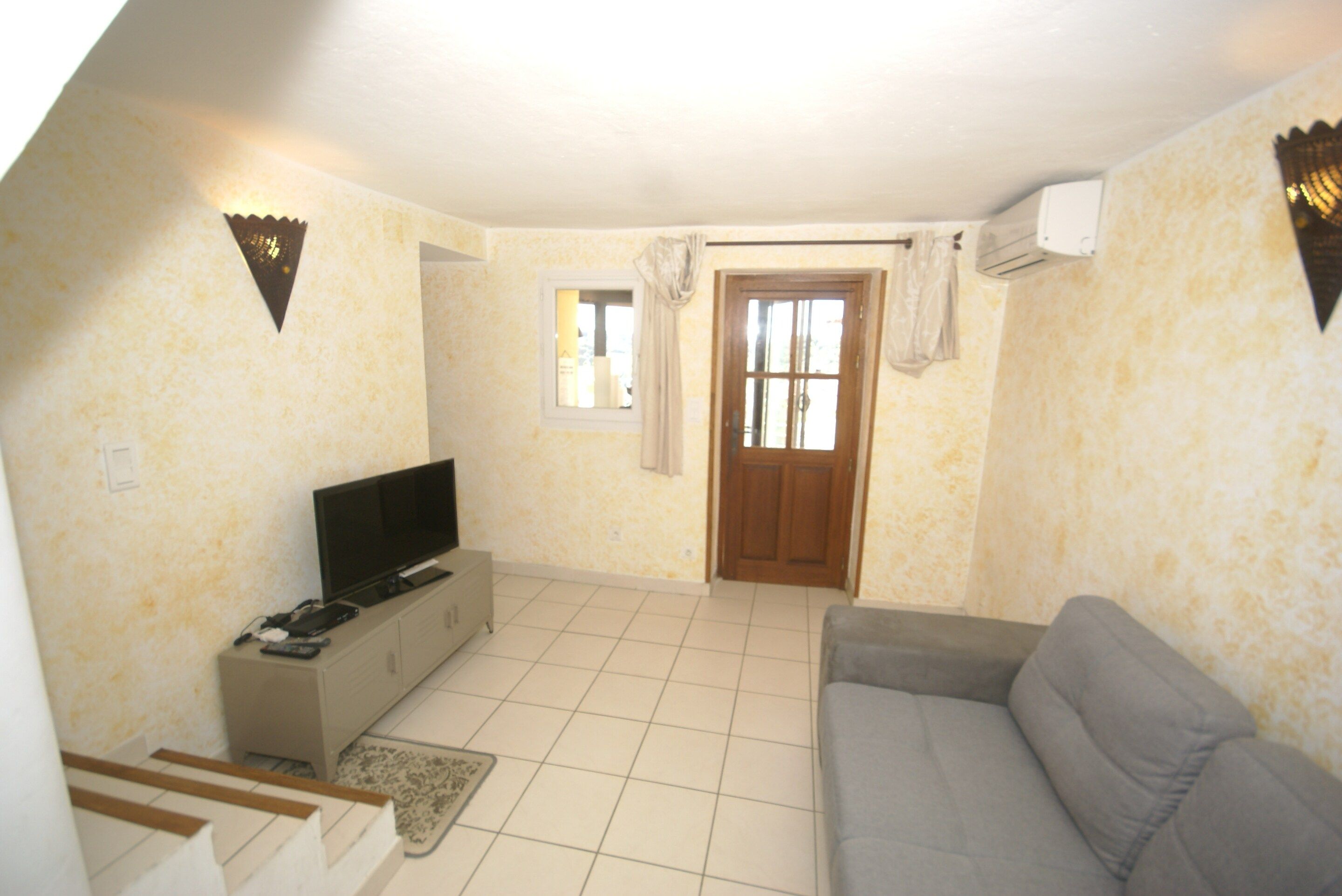 A living room with a television on a cabinet, a sofa, a door, and a window.