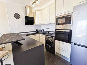 Een moderne keuken met een centraal eiland, inbouwapparatuur en een hangend horloge.