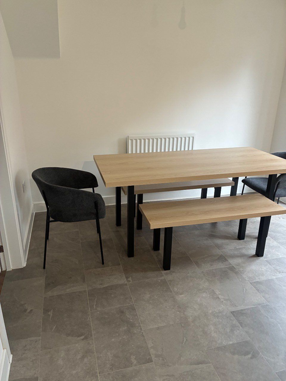 A dining area with a wooden table and two chairs, a bench, and a radiator.
