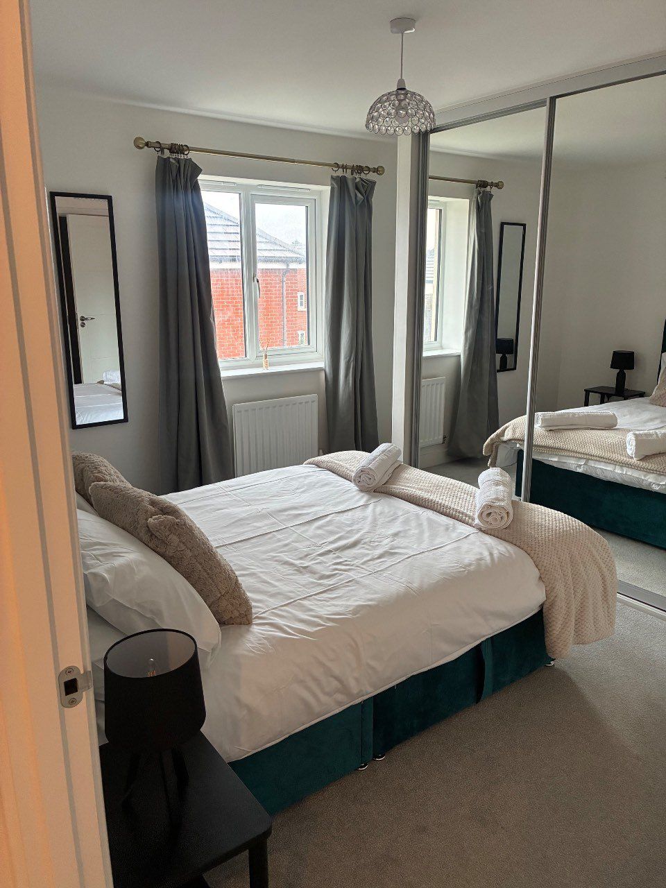 A bedroom with a large bed, a mirror, a window with curtains, and a radiator.