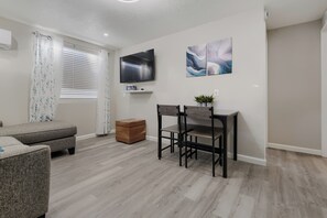 Ein modernes Wohnzimmer mit einer Couch, einem Esstisch mit Stühlen, einem Fernseher und Kunstwerken an der Wand.