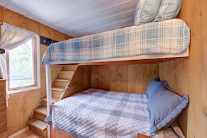 Un lit superposé avec une couverture à carreaux et des oreillers, des murs en bois, une fenêtre avec des rideaux et un escalier.