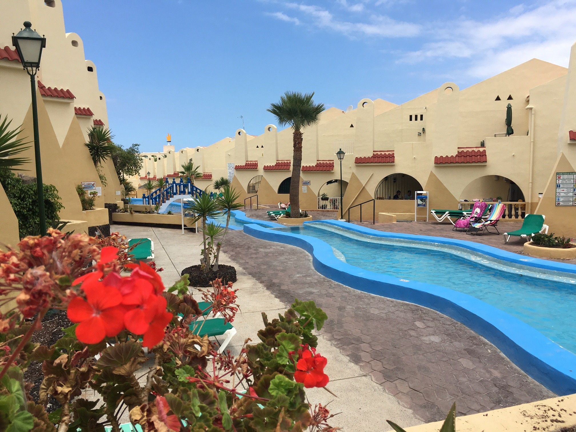 A resort pool area with a winding pool, palm trees, and lounge chairs.