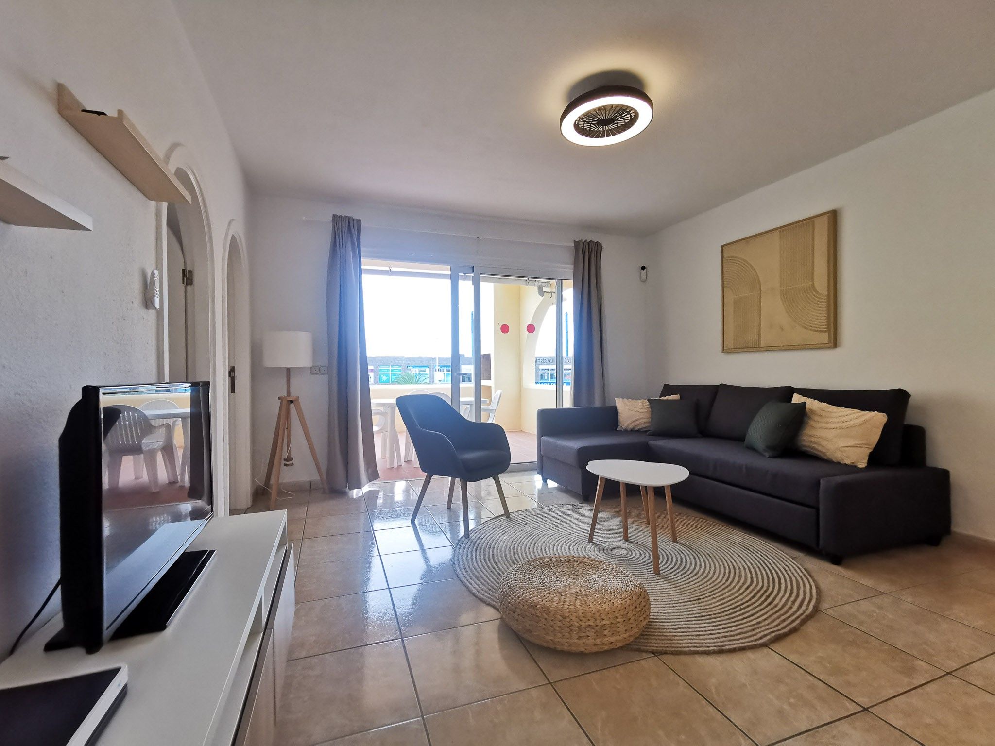Un salon moderne avec un canapé, un téléviseur, une lampe et une vue sur l’extérieur.