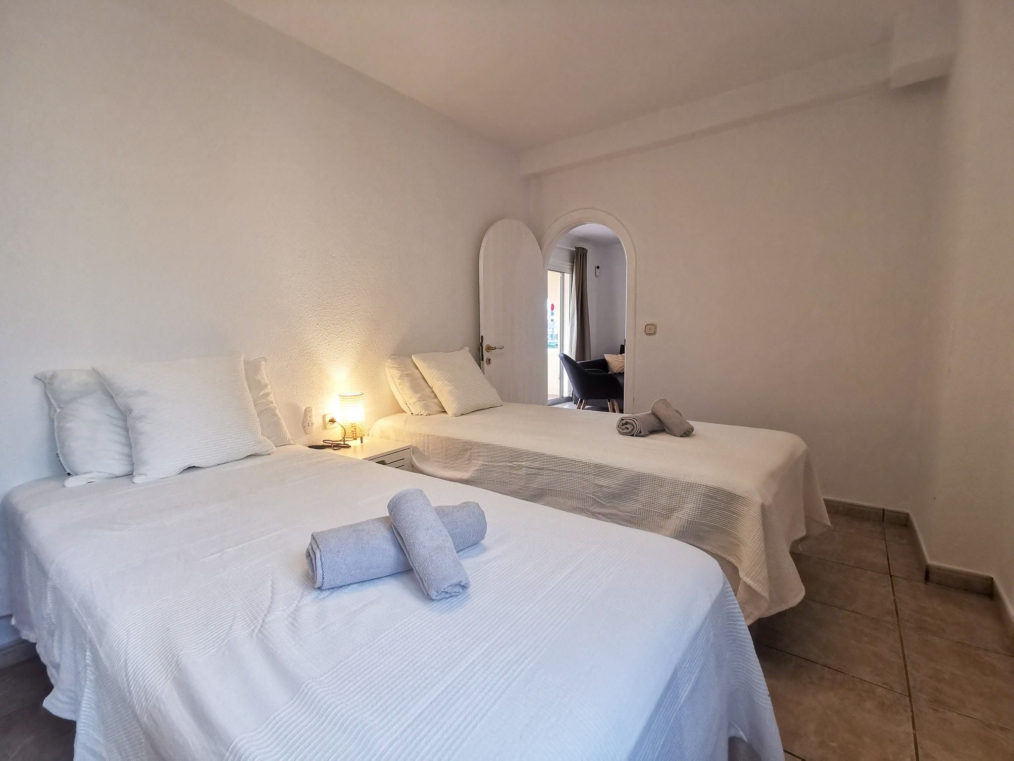 Een hotelkamer met twee bedden, een nachtkastje met een lamp, en een badkamer zichtbaar door een boogvormige deuropening.