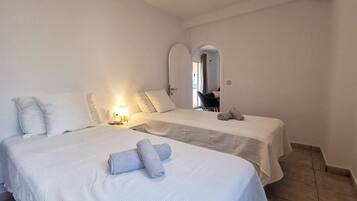 Een hotelkamer met twee bedden, een nachtkastje met een lamp, en een badkamer zichtbaar door een boogvormige deuropening.
