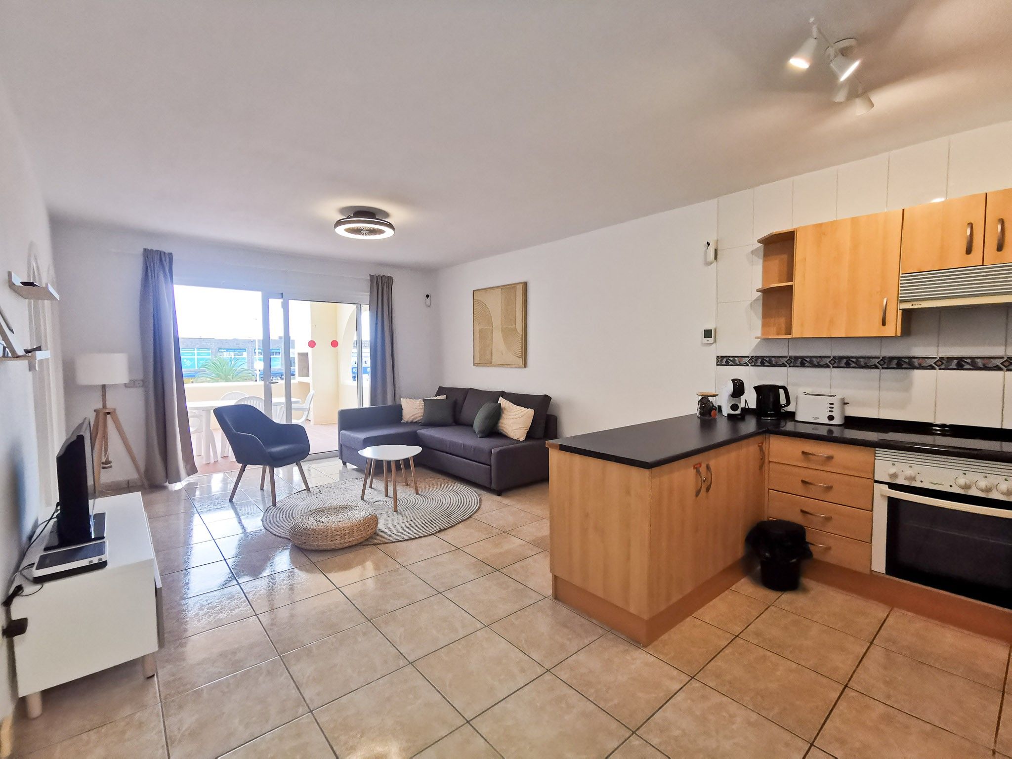 Een moderne keuken met een centraal eiland, een zithoek met een bank en stoelen, en een uitzicht door een glazen deur.