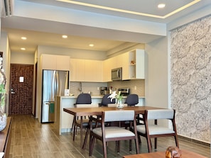 Ett modernt kök med vita skåp, ett kylskåp i rostfritt stål och en mikrovågsugn. Det finns en matplats med ett bord och stolar i trä.