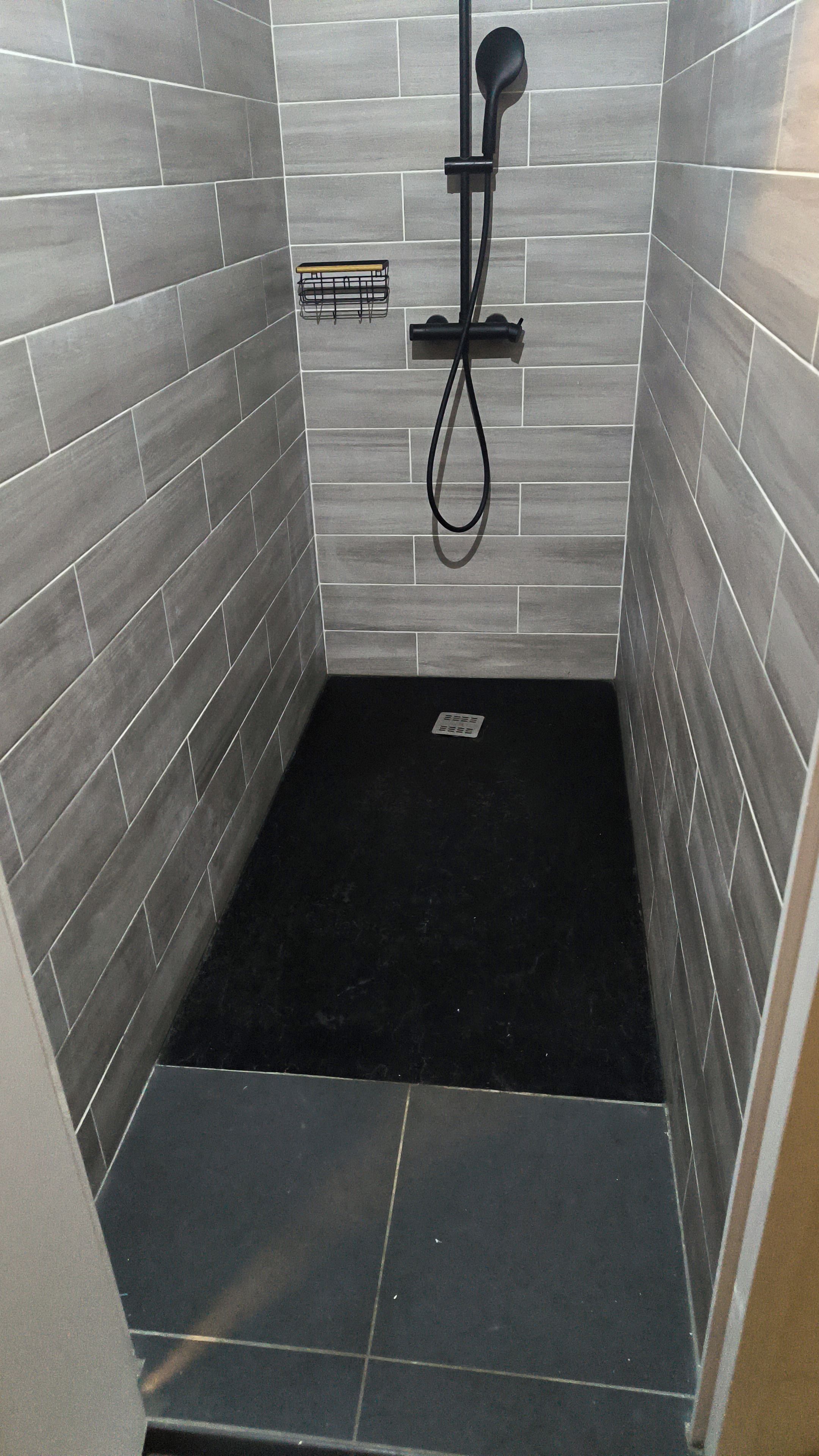 A small, enclosed shower area with grey tiles and a black floor.
