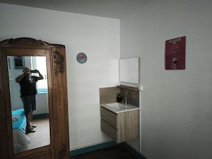 Une salle de bain avec une porte en bois, un miroir, un lavabo et une étagère fixée au mur.