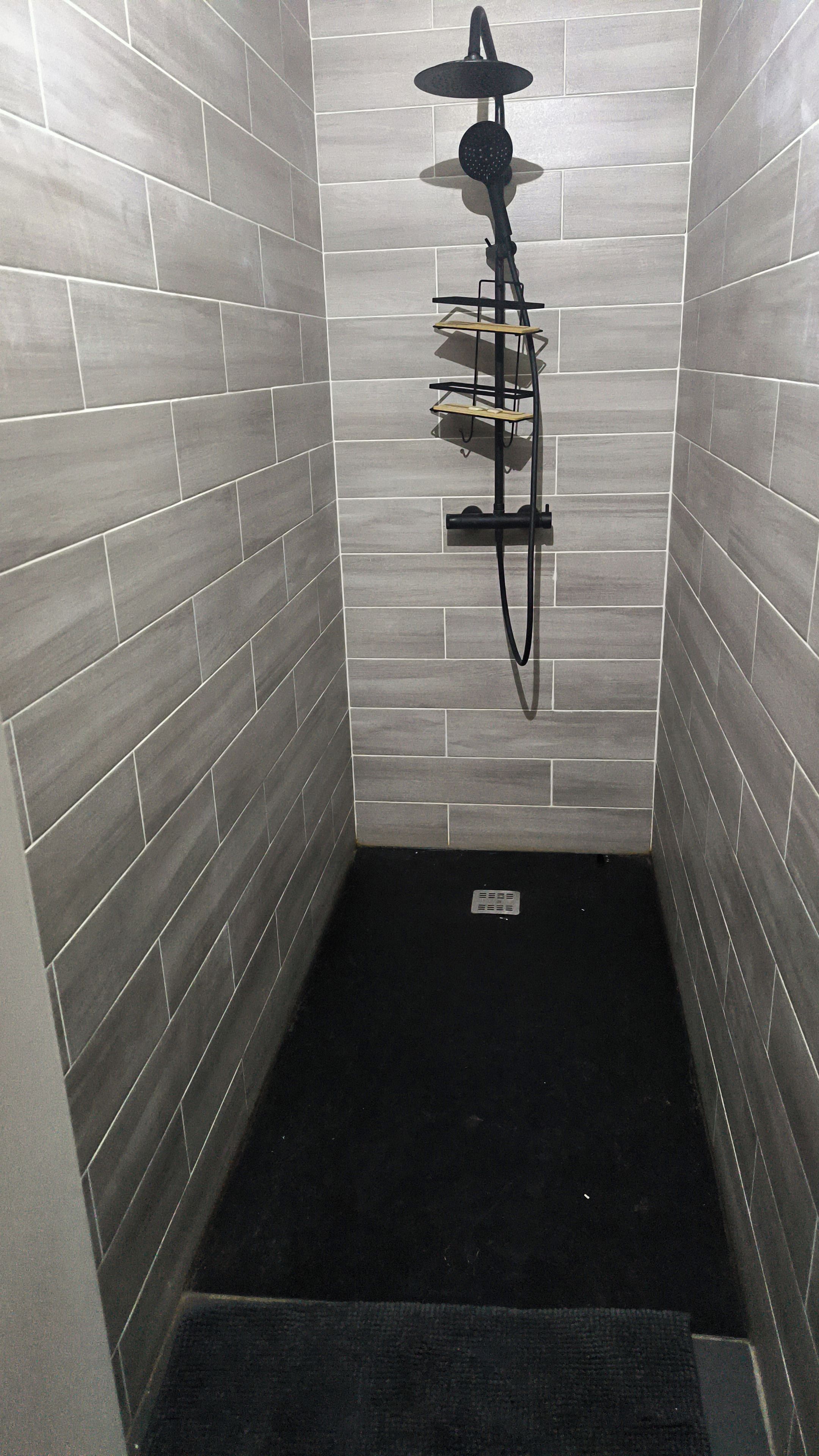 A shower area with grey tiles, a black showerhead, and a black mat.