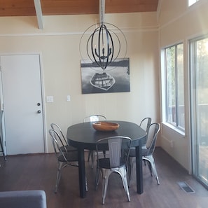 A dining area with a round table, six chairs, a central light fixture, and a painting on the wall. - Tranquil 3-bedroom cabin with AC in charming Groveland (Groveland)