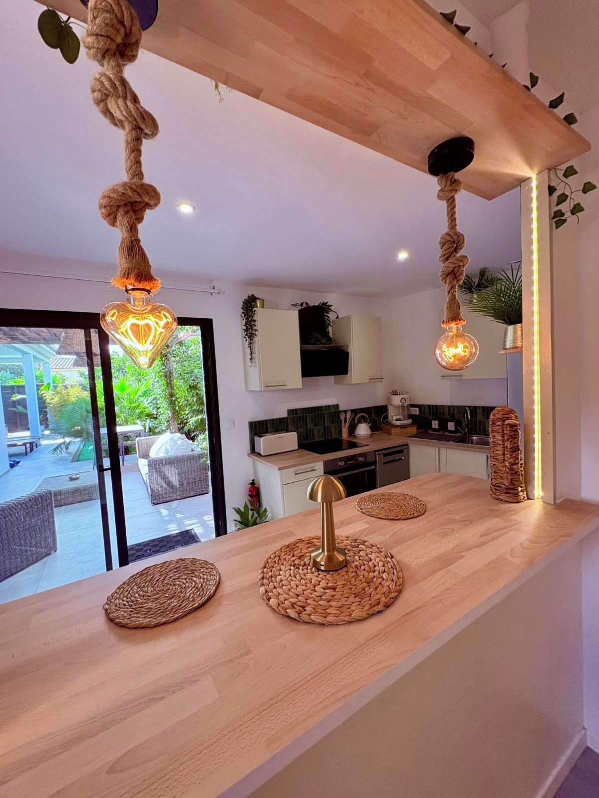 A modern kitchen with a wooden countertop, hanging rope lights, and a view of the outdoor patio.