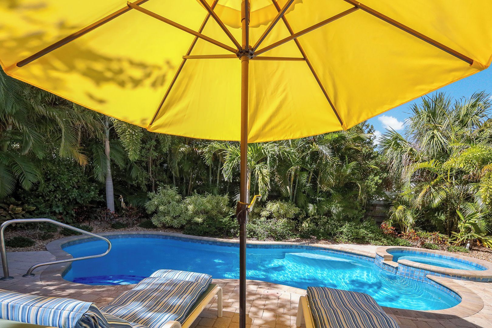 Une piscine agrémentée d’un parasol jaune, de chaises longues et d’une végétation tropicale.