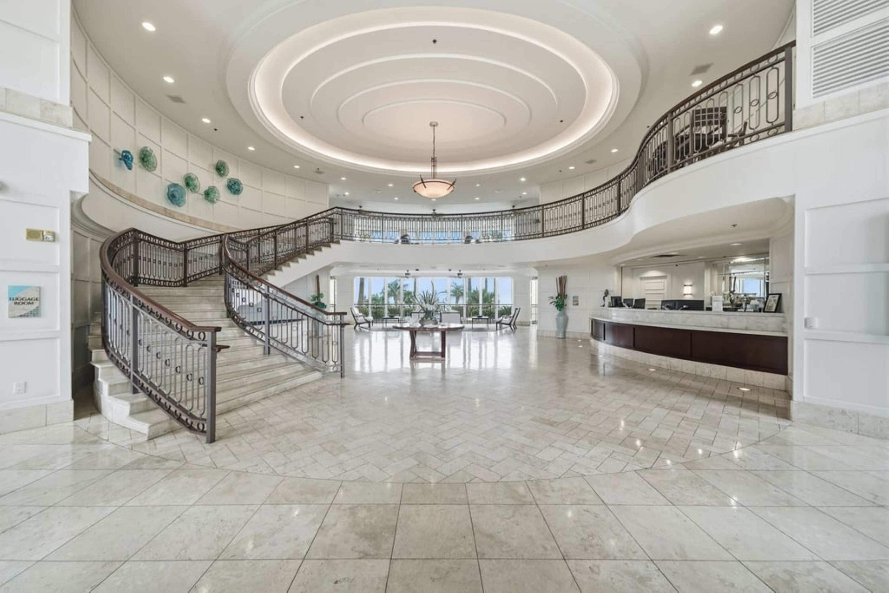 Eine großzügige Lobby mit einer imposanten Treppe, einem Empfangsbereich und Blick ins Freie.