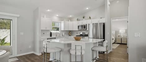 A modern kitchen with white cabinetry, a central island with bar stools, stainless steel appliances, and recessed ceiling lighting.