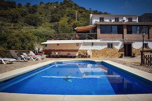 Une piscine avec des chaises longues, un mur en pierre et un bâtiment doté d’un balcon.