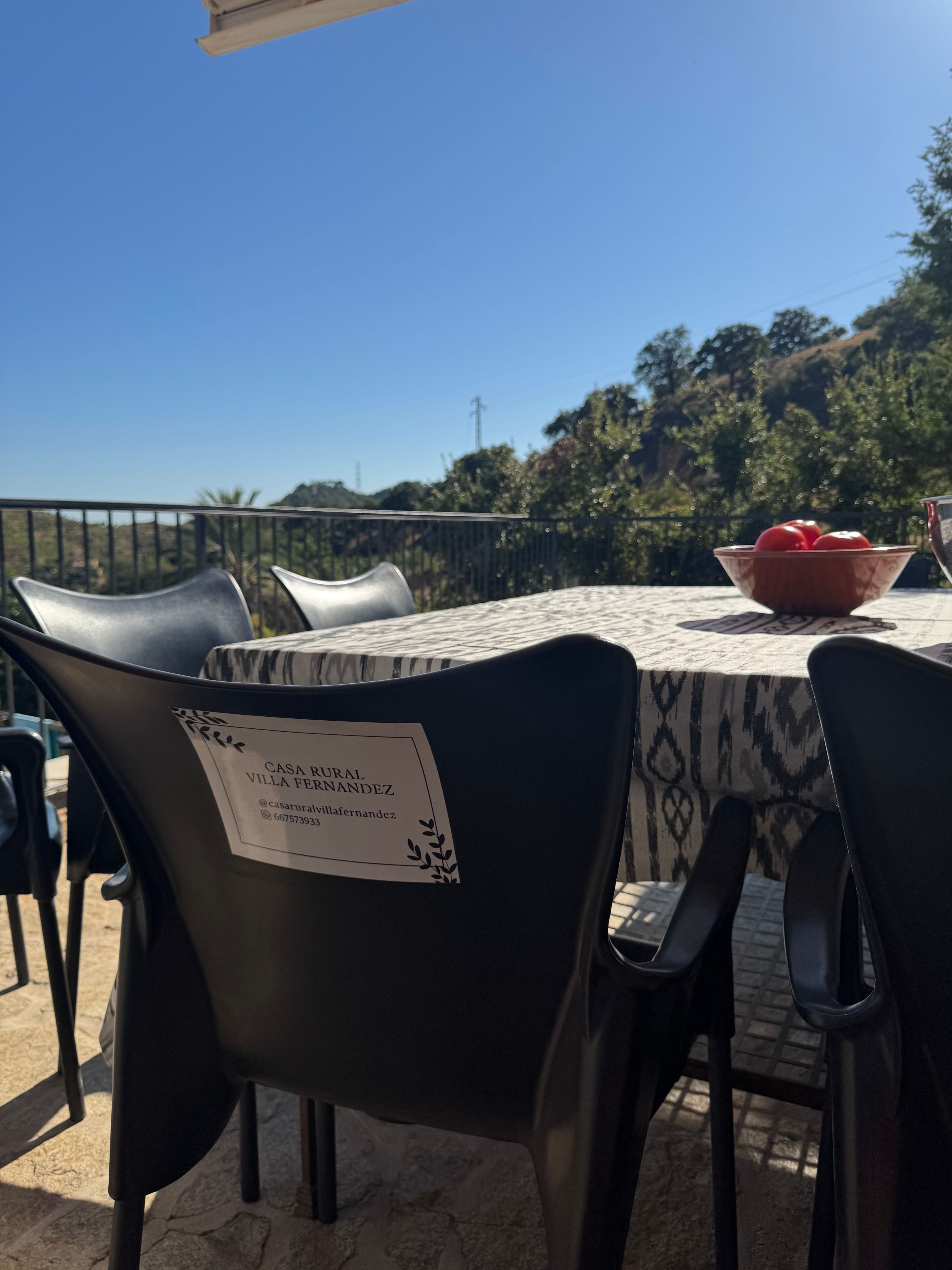 Un espace extérieur aménagé pour les repas, avec une table et des chaises, une enseigne indiquant le nom de l'établissement et ses coordonnées, et une vue sur le paysage environnant.
