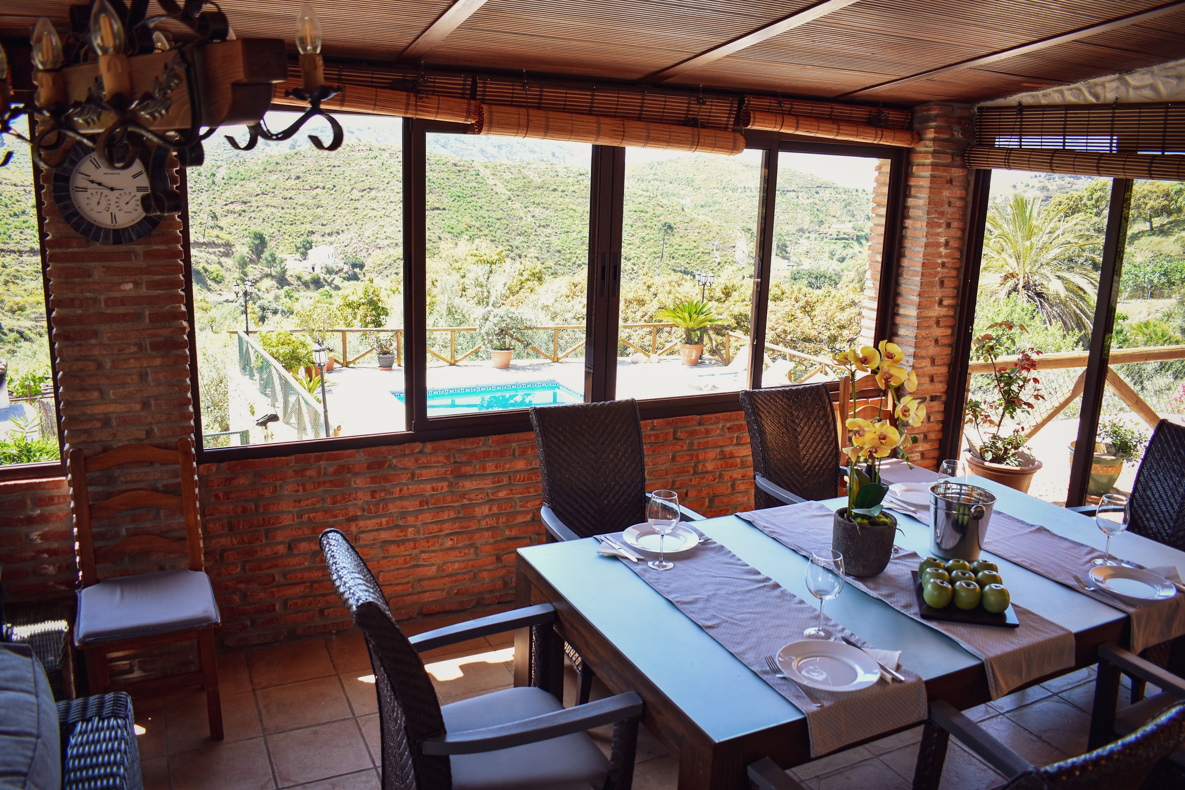 Un coin repas avec une table dressée pour deux personnes, de grandes fenêtres donnant sur un paysage vallonné et un mur en briques.