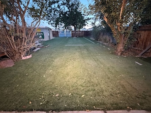 A well-maintained grassy area with a wooden fence, trees, and a building with an 'EXIT' sign. - Capitol Outpost Hot Tub Pet friendly fenced Yard fire pit (Carson City)
