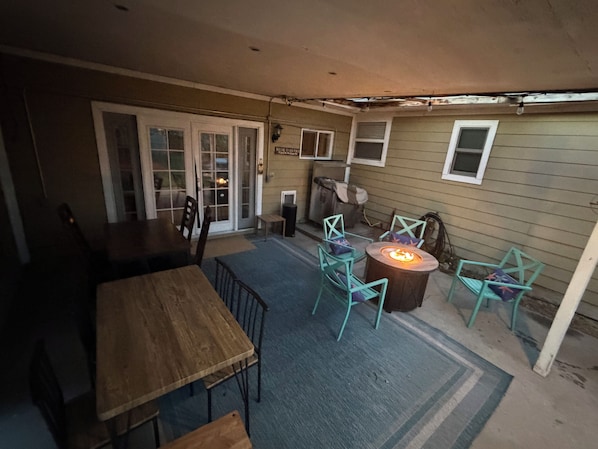 A covered patio with a wooden table and chairs, a fire pit, and a blue rug. - Capitol Outpost Hot Tub Pet friendly fenced Yard fire pit (Carson City)