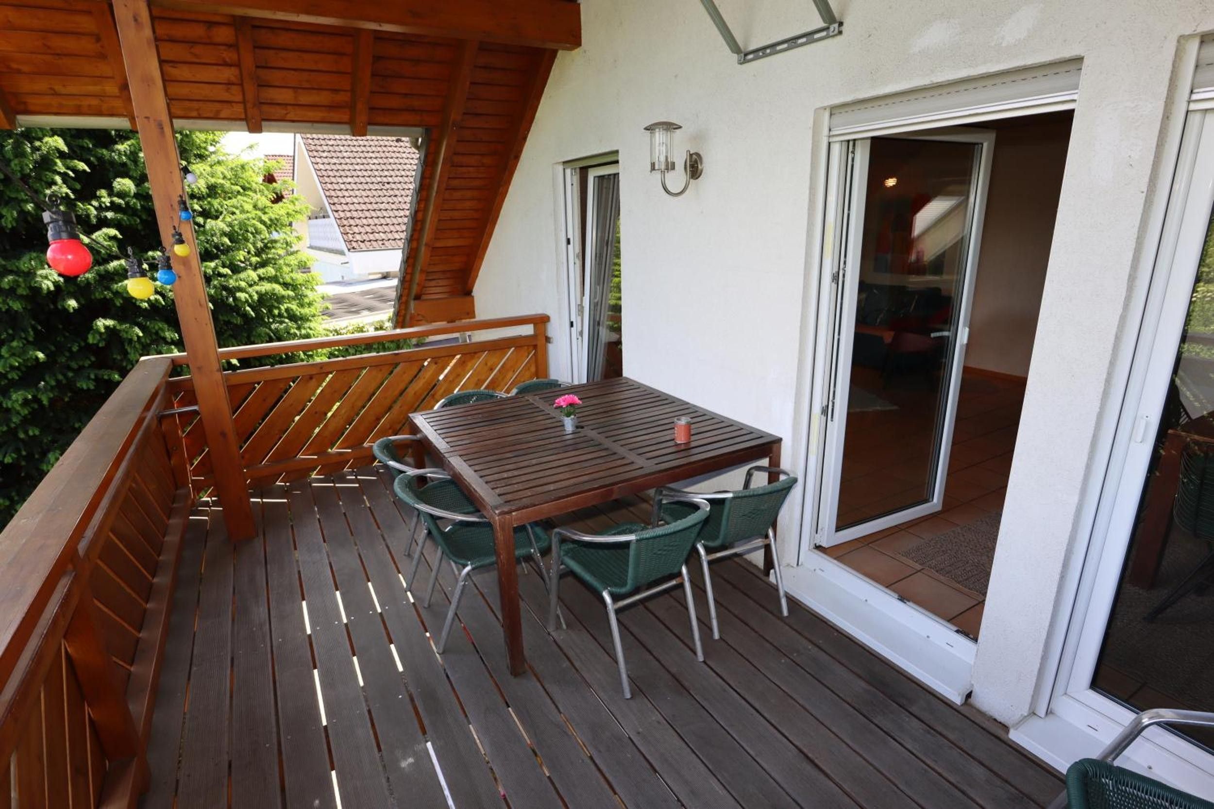 A wooden deck with a table and chairs, a railing, and a sliding glass door leading to an interior space.