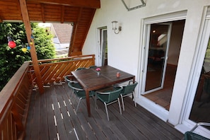 Een houten terras met een tafel, stoelen, een leuning en een schuifdeur naar de binnenruimte.