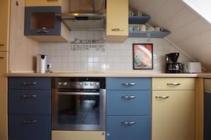 Een keuken met een inbouwoven, een koffiezetapparaat en een betegelde spatwand.