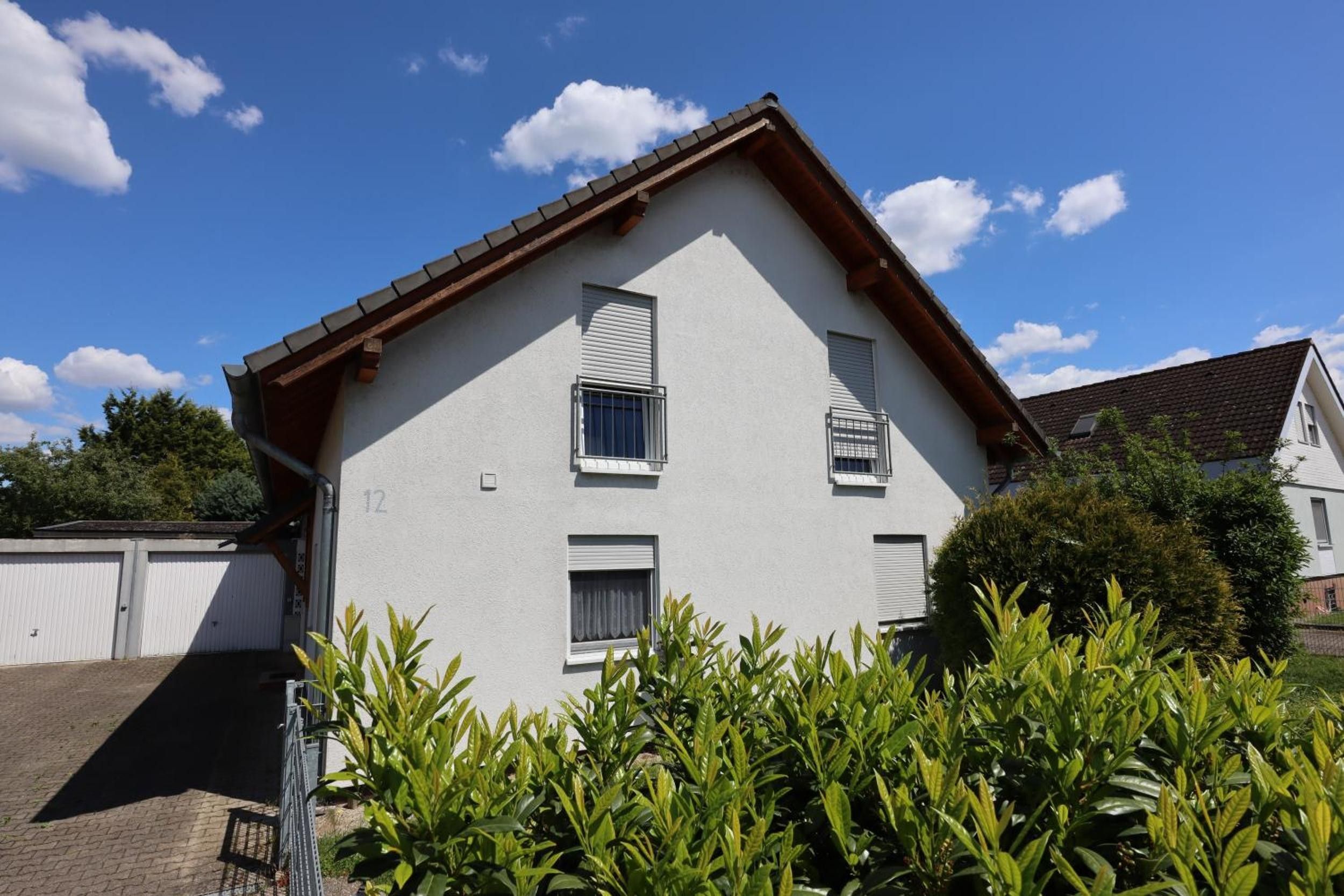 Un bâtiment à deux étages, doté d’un toit à pignon, d’un garage et d’un jardin bien entretenu en premier plan.