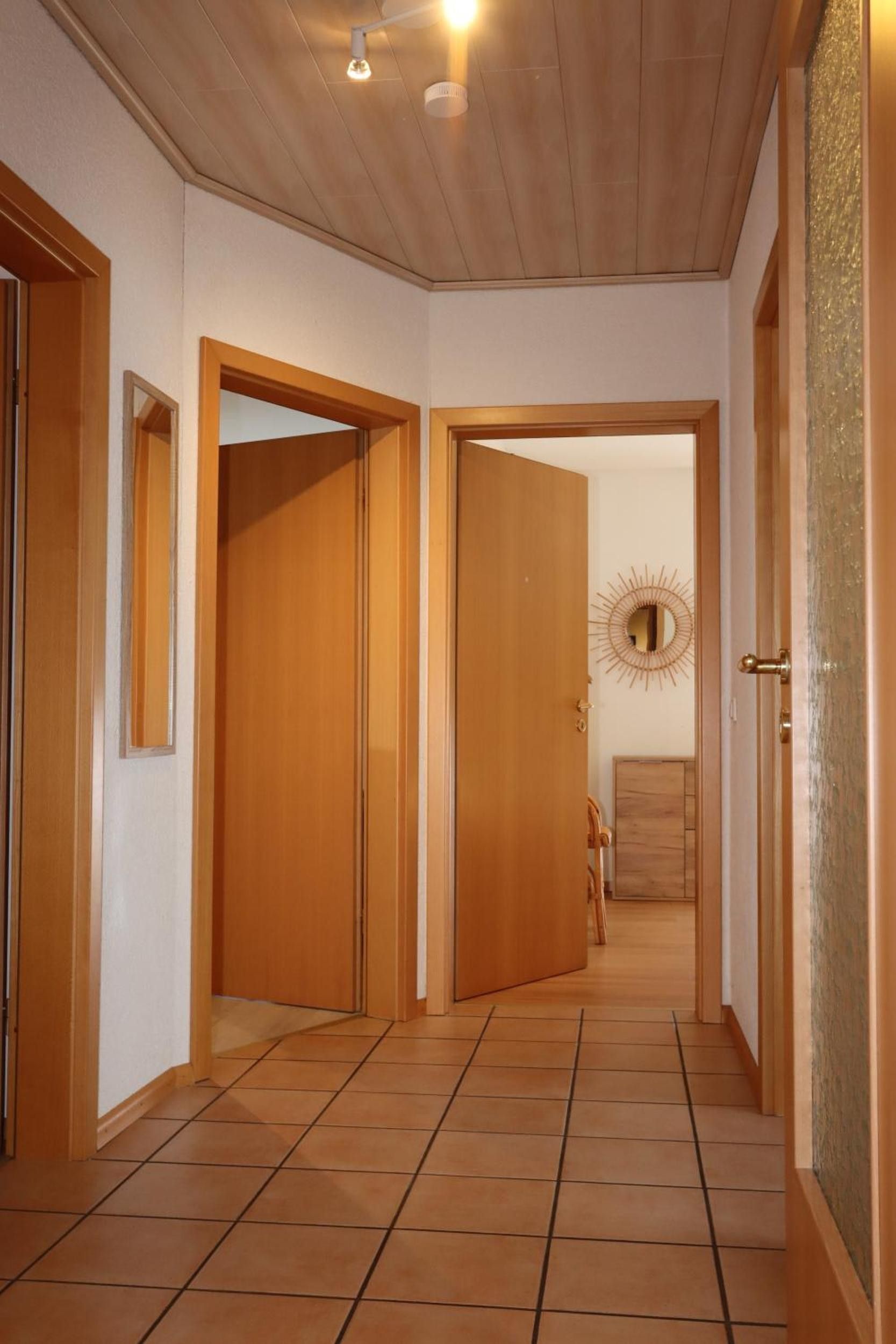 A hallway with wooden doors, a mirror, and a sunburst wall decoration.