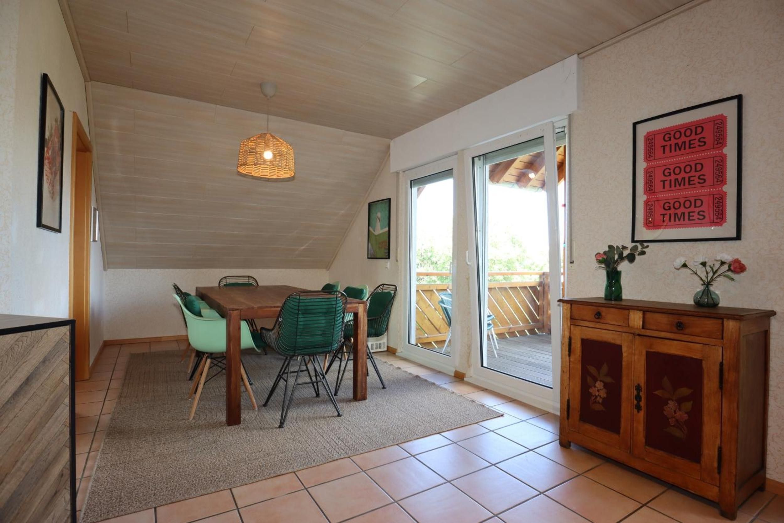 A dining area with a wooden table and chairs, a hanging light fixture, a sliding glass door leading to an outdoor deck, and a cabinet with floral designs.