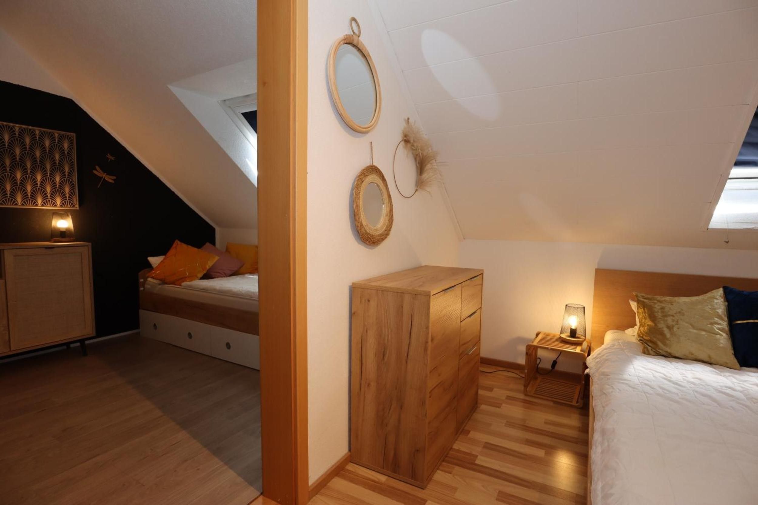 Une chambre avec un plafond en pente, un lit avec des oreillers, une commode en bois et des miroirs fixés au mur.