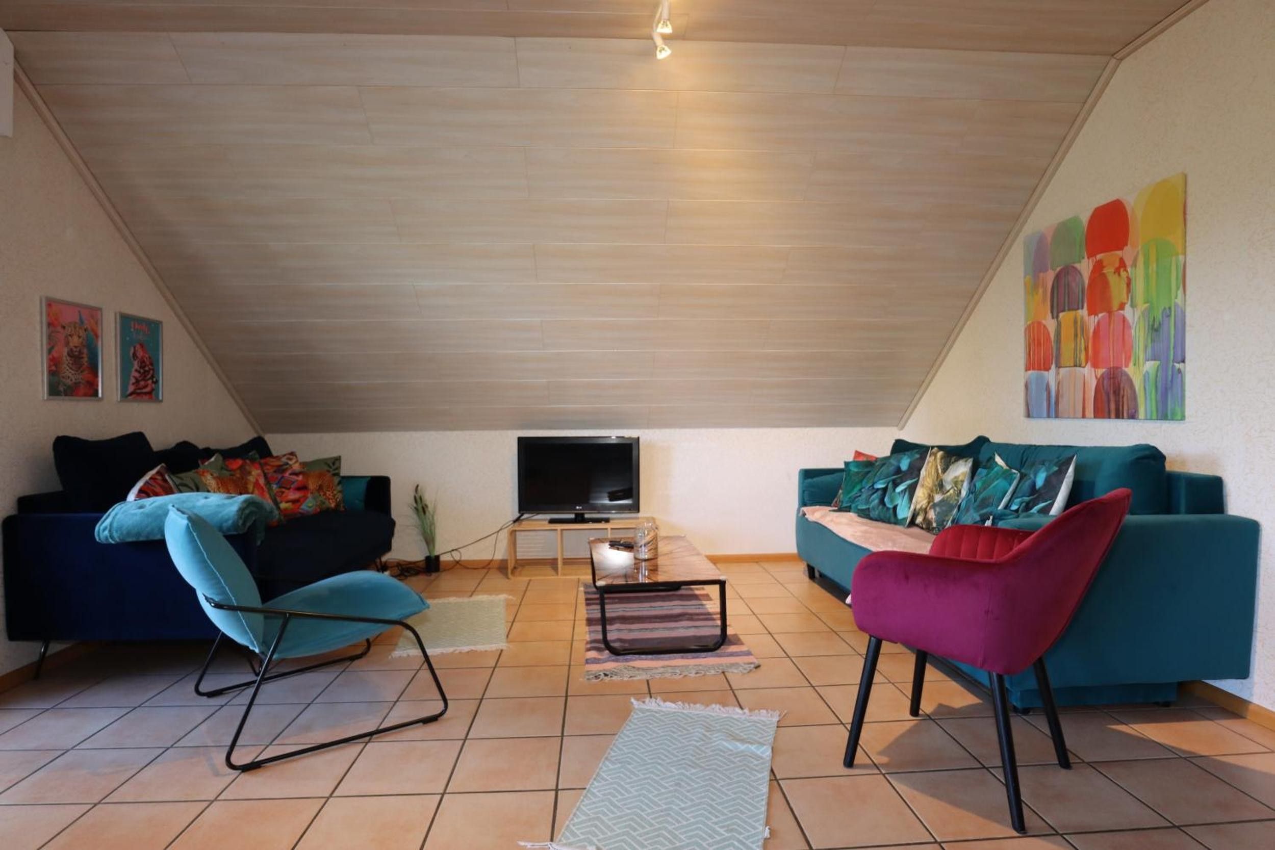 Un vaste espace de vie doté d’un plafond en pente, de deux canapés, d’un téléviseur et d’un tableau abstrait aux couleurs vives accroché au mur.
