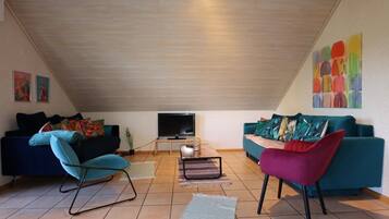 Un vaste espace de vie doté d’un plafond en pente, de deux canapés, d’un téléviseur et d’un tableau abstrait aux couleurs vives accroché au mur.