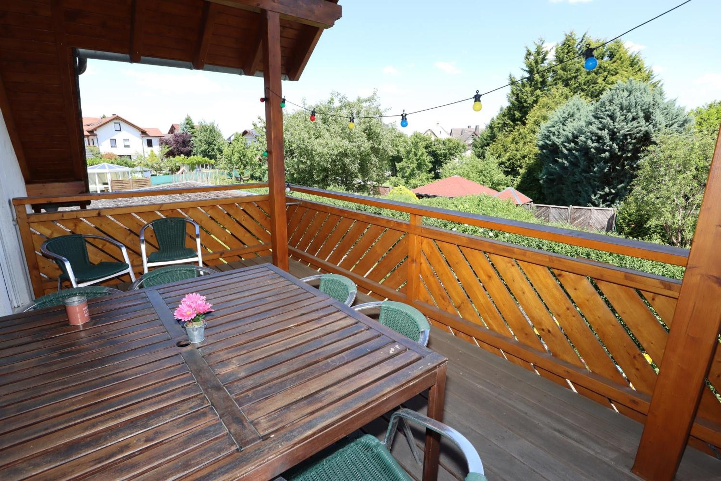 Une terrasse en bois avec une table et des chaises, donnant sur un quartier résidentiel bordé d’arbres et de maisons.