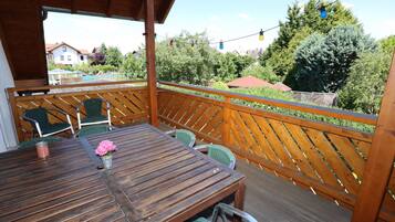 Une terrasse en bois avec une table et des chaises, donnant sur un quartier résidentiel bordé d’arbres et de maisons.