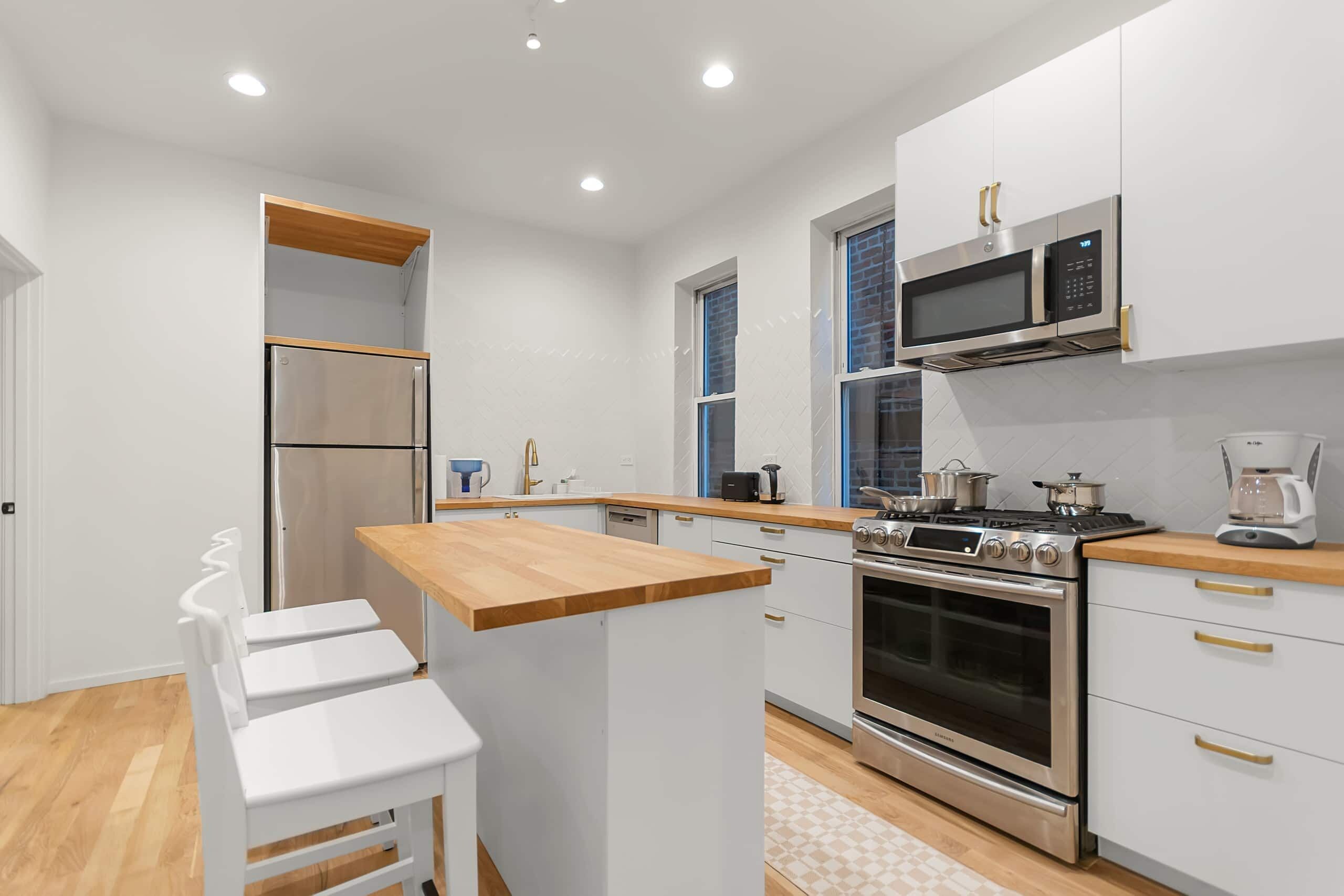 A modern kitchen with stainless steel appliances, a wooden countertop, and white cabinetry.