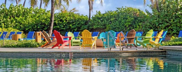 Un área junto a la piscina con varias sillas Adirondack de colores dispuestas en fila.