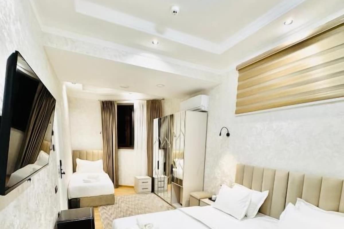 A hotel room with a large bed, a flat-screen TV mounted on the wall, a bedside table, and a mirror.
